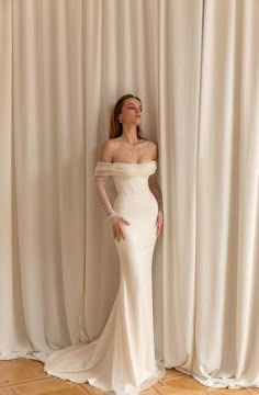 a woman standing in front of a curtain wearing a white dress