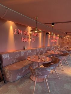 an empty restaurant with pink walls and wooden tables in the foreground is lit by neon lights