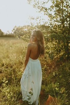 a woman in a white dress standing in tall grass with her back to the camera