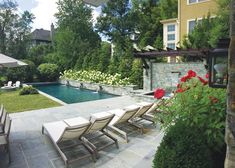 an outdoor pool with lounge chairs next to it and flowers in the foreground, surrounded by greenery