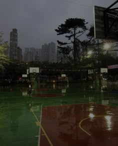 an empty basketball court in the middle of a city at night with lights shining on it