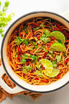 a bowl filled with noodles and vegetables on top of a table next to sliced limes