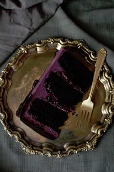 a piece of chocolate cake on a silver plate with a fork and knife next to it