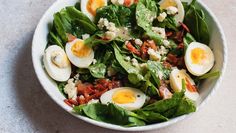 a salad with hard boiled eggs, bacon and lettuce in a white bowl