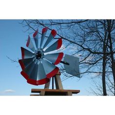 a large metal windmill sitting on top of a wooden table next to a bare tree