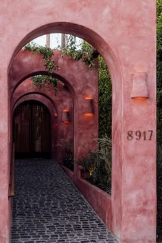 an archway leading into a pink building with plants growing on the walls and walkways