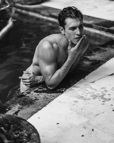 a shirtless man sitting on the edge of a pool with his hands in his mouth