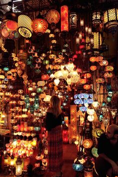 a woman standing in front of a store filled with lots of lanterns and lights hanging from the ceiling