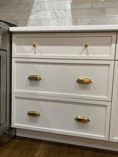 a kitchen with white cabinets and gold pulls on the drawers, next to a stainless steel dishwasher