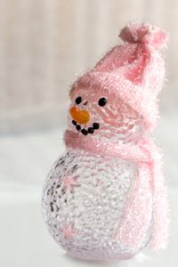 a small pink snowman ornament sitting on top of a white tablecloth