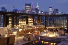 an outdoor bar overlooking the city skyline at night with lit candles on tables and chairs