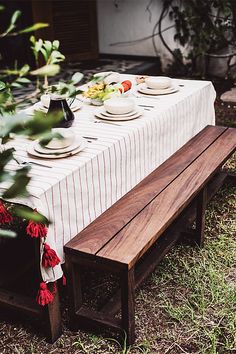 a wooden bench sitting in the grass near a table with plates and cups on it