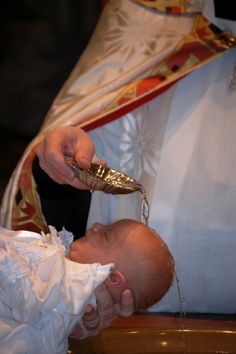 a baby is being given water from a priest's hand as it sits in front of him