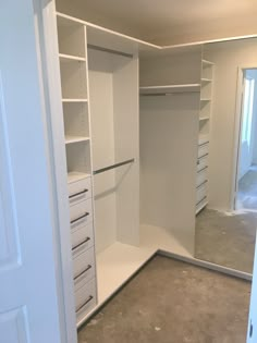 an empty walk in closet with white shelves and drawers on each side, doors open to reveal another room