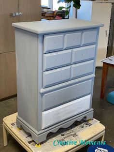 a white dresser sitting on top of a wooden table next to a blue planter