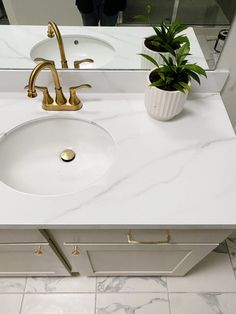 a bathroom vanity with a white marble counter top and gold faucet, along with a potted plant