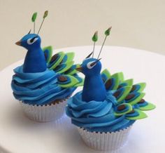 two cupcakes with blue frosting and green leaves on top are decorated like peacocks