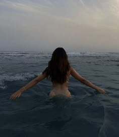 a woman is in the water with her arms spread out and looking at the sky