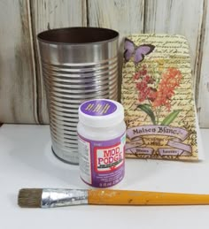 some paint and a brush sitting on a table next to a tin with flowers in it