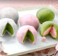 four different types of doughnuts on a white tray with pink and green frosting