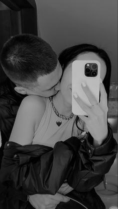 black and white photograph of a man kissing a woman's face on her phone