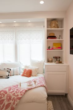 a white bed sitting in a bedroom next to a window with lots of pillows on top of it