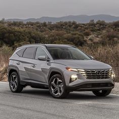 the front end of a gray suv driving down a road