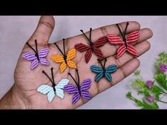 small crocheted butterflies are being held in someone's hand with flowers behind them