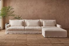 a living room with a couch, ottoman and potted plant on the floor in front of a window