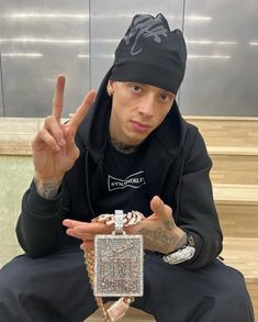 a man sitting on the ground holding up his peace sign and wearing a black hoodie