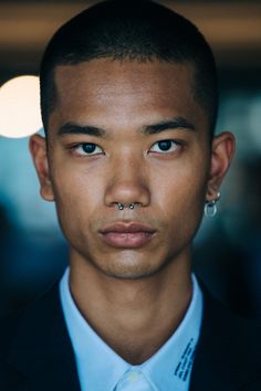 a close up of a person wearing a suit and tie with piercings on his nose