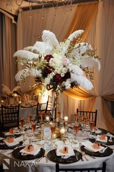 a tall vase filled with white flowers and feathers on top of a dining room table