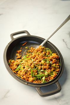 a skillet filled with food on top of a white counter next to a spoon