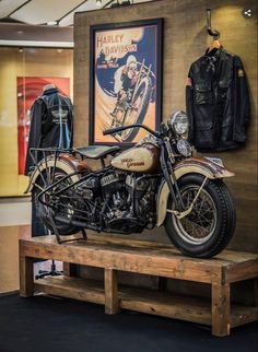 an old motorcycle is on display in a museum with leather jackets hanging from the ceiling