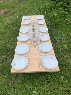 a long table with plates and glasses on it in the middle of a grassy field