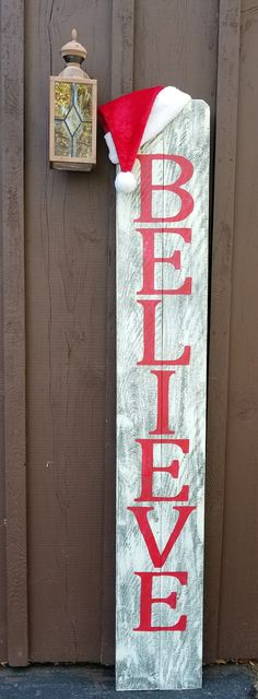 a wooden sign that says believe hanging on the side of a building with a santa hat on it