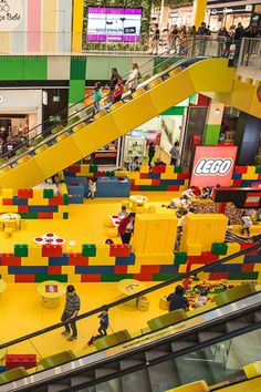 an escalator in a shopping mall with legos on the floor and people walking around