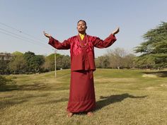 a man standing in the grass with his hands out and wearing a long red robe