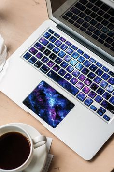 an open laptop computer sitting on top of a wooden table next to a cup of coffee