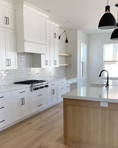 an empty kitchen with white cabinets and black lights hanging over the stove top, along with wooden flooring