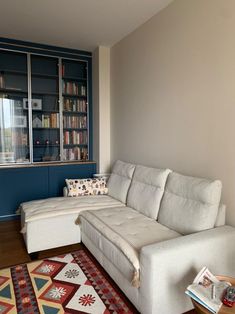 a living room with a white couch and bookshelf in the corner, next to a red rug