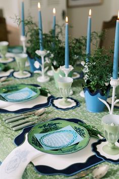 the table is set with blue and green plates, silverware, and candle holders