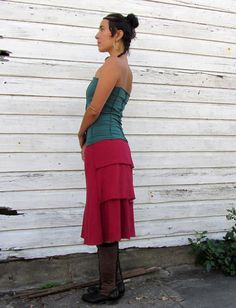 a woman standing in front of a white wall wearing a red skirt and brown boots