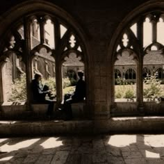 two people sitting on a bench in an old building with arched windows and stone flooring