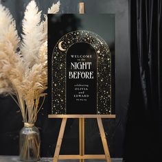 a black and gold welcome sign sitting on top of a wooden easel next to some pamy plants