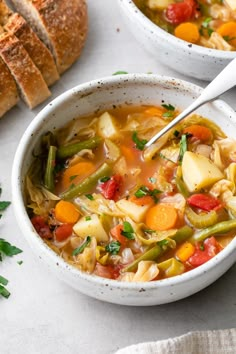 two bowls filled with vegetable soup next to a loaf of bread