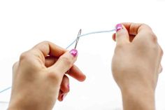 the woman is knitting with her hands while she holds on to something blue and pink