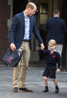 a man holding the hand of a little boy who is walking down a street with a bag