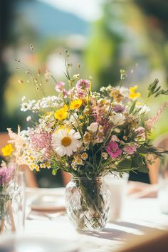 a vase filled with lots of flowers sitting on top of a table next to two glasses