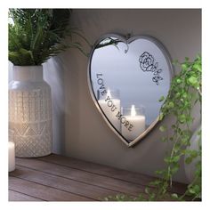 a heart shaped mirror hanging on the side of a wall next to a vase with candles